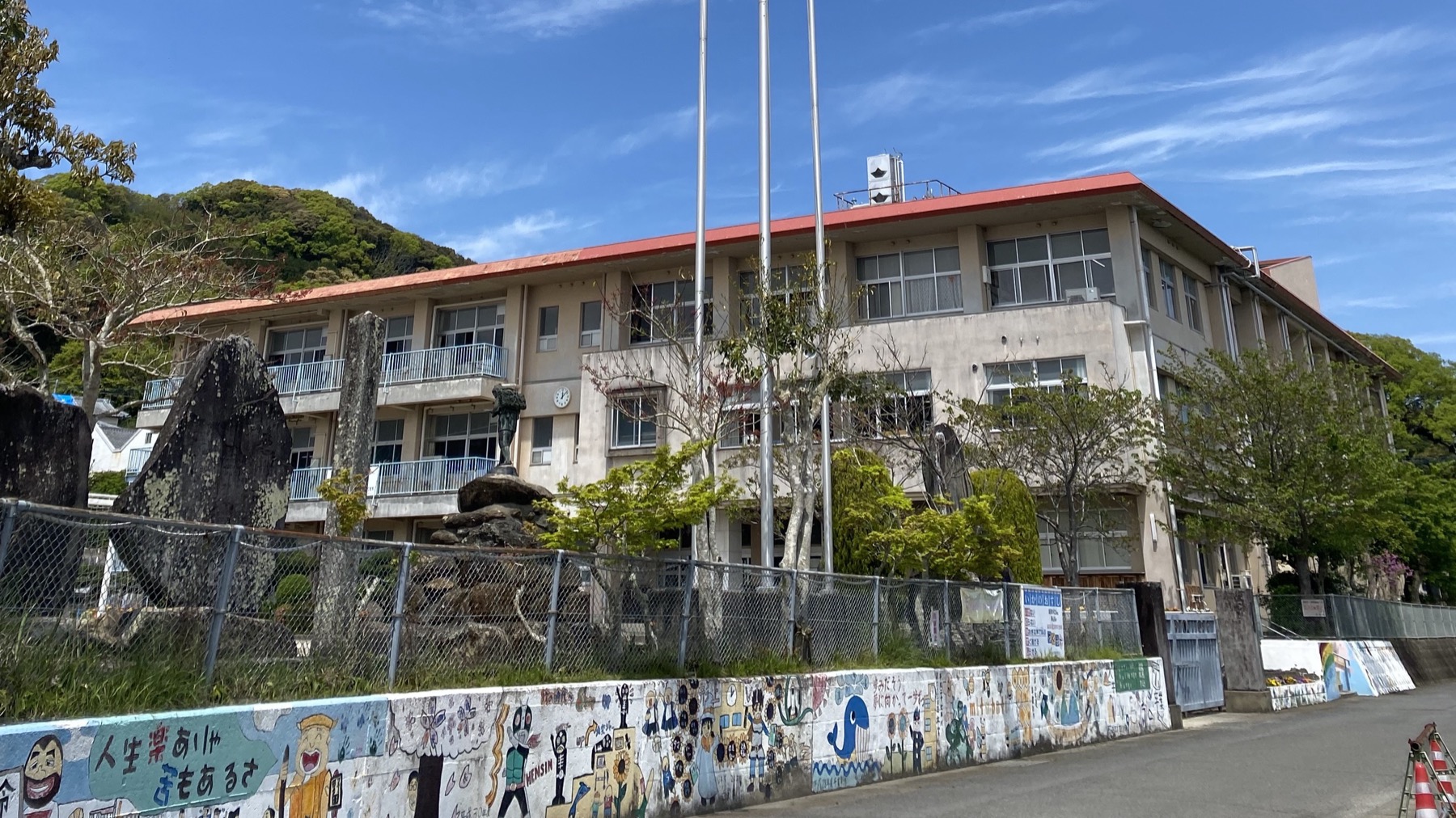 形上小学校の校舎。赤い屋根と三階建ての校舎、手前のフェンスと、子どもたちの絵がならぶ塀