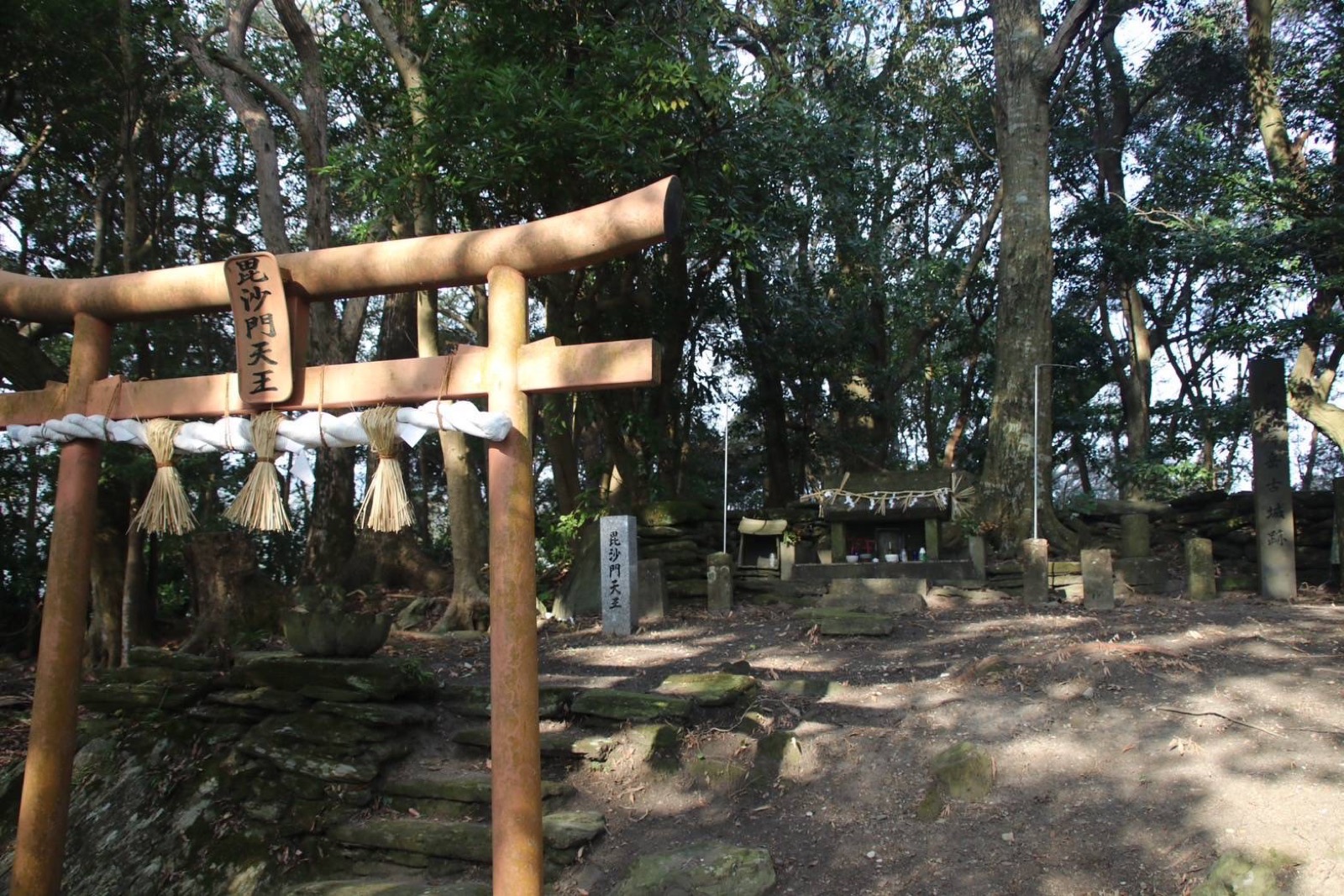 舞岳城跡。毘沙門天王の鳥居と石碑が立ち、木立の奥に小さなお社が見える